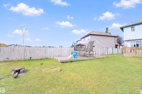 Expansive rear yard featuring a wooden privacy fence, a raised wooden deck, and a defined fire pit area - 15911 38 Street Nw, Edmonton, AB 