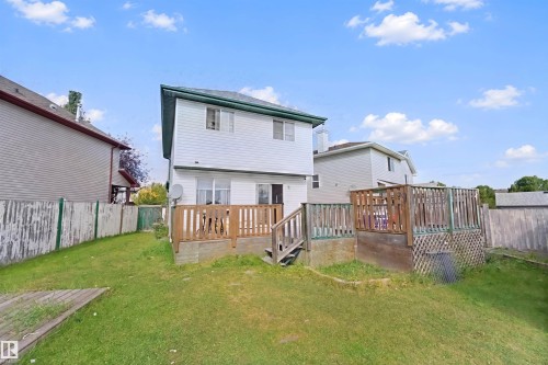 Expansive backyard with a two-story residence featuring white siding, a green roof, and a two-tiered wooden deck - 15911 38 Street Nw, Edmonton, AB 