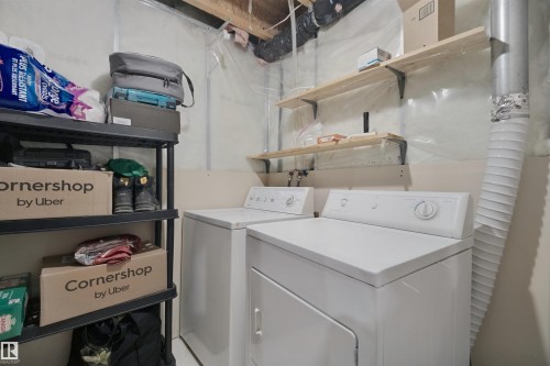White washer and dryer appliances, exposed ceiling joists, and open wood shelving - 15911 38 Street Nw, Edmonton, AB 