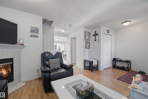 Living area featuring wood-finish flooring, a fireplace with a light-toned tile surround, a built-in closet with bifold doors, and a staircase with white railings - 15911 38 Street Nw, Edmonton, AB 