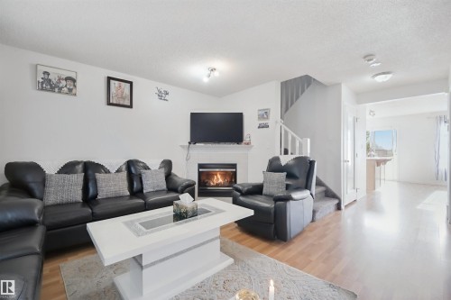 Living area featuring wood-finish flooring, a fireplace with a white mantel, and a staircase with white railings - 15911 38 Street Nw, Edmonton, AB 