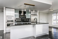 Modern kitchen featuring an integrated stainless steel appliance suite, black countertop island with sink, white high-gloss cabinetry, and pendant lighting - 