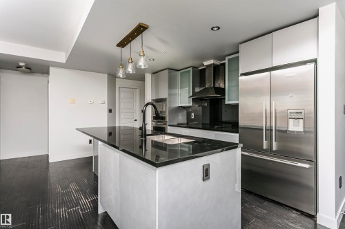 Kitchen featuring an island with a black countertop, stainless steel appliances, dark wood-finish flooring, and white cabinetry - #1902 10388 105 St Nw, Edmonton, AB 