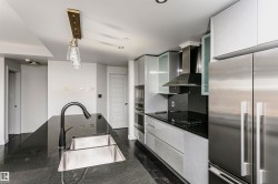 Kitchen featuring a central island with a double basin sink and gooseneck faucet, light gray flat-panel cabinetry, stainless steel appliances, and dark countertops - 