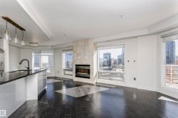 Dark wood-finish flooring, built-in fireplace with stone surround, large windows, kitchen island with black countertop, and pendant lighting - 