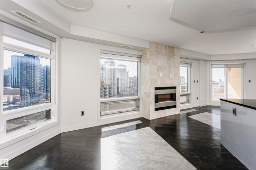Expansive windows, built-in fireplace with stone surround, dark wood-finish flooring, and white recessed lighting - #1902 10388 105 St Nw, Edmonton, AB 
