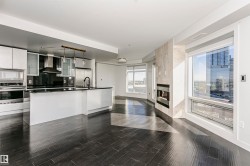 Modern kitchen featuring white cabinetry, black countertops, stainless steel appliances, and a central island with pendant lighting - 