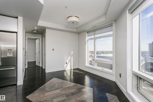 Wood-finish flooring, recessed ceiling lighting, tray ceiling detail, large windows with roller shades, and a stainless steel refrigerator - #1902 10388 105 St Nw, Edmonton, AB 