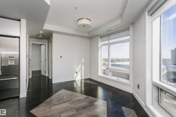 Wood-finish flooring, recessed ceiling lighting, tray ceiling detail, large windows with roller shades, and a stainless steel refrigerator - 