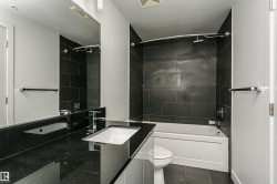 Bathroom featuring a built-in tub with a tile surround, dark tile flooring, a large vanity mirror, and a sleek vessel sink with chrome fixtures - 