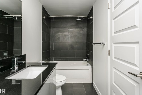Bathroom featuring a deep soaking tub with subway tile surround, a sleek vanity with an integrated sink, a contemporary chrome faucet, and a panel-style interior door - #1902 10388 105 St Nw, Edmonton, AB 