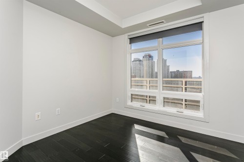 Dark wood-finish flooring, white walls, large window with roller shade, and tray ceiling detail - #1902 10388 105 St Nw, Edmonton, AB 