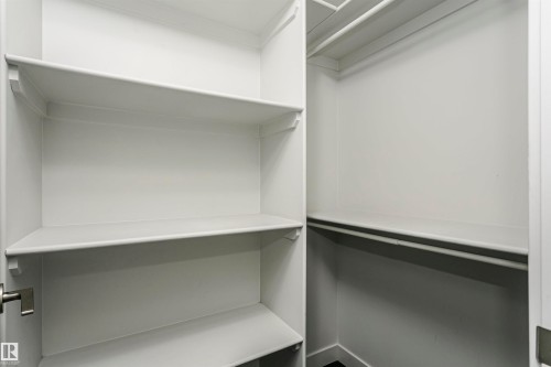 Walk-in closet featuring white built-in shelving, white walls, and closet rods - #1902 10388 105 St Nw, Edmonton, AB 