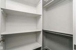 Walk-in closet featuring white built-in shelving, white walls, and closet rods - 