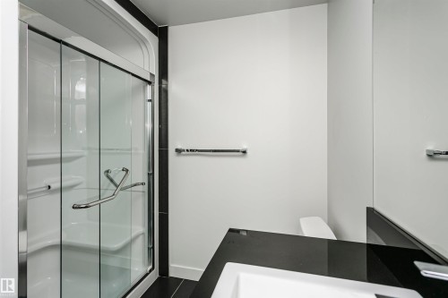 Glass-enclosed shower with integrated seating, chrome fixtures, and a sleek black countertop - #1902 10388 105 St Nw, Edmonton, AB 
