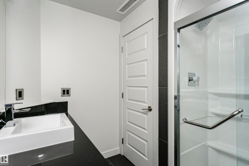 Bathroom featuring a dark countertop with an integrated rectangular basin, chrome faucet, and glass-enclosed shower with a rainfall showerhead - #1902 10388 105 St Nw, Edmonton, AB 