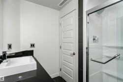Bathroom featuring a dark countertop with an integrated rectangular basin, chrome faucet, and glass-enclosed shower with a rainfall showerhead - 