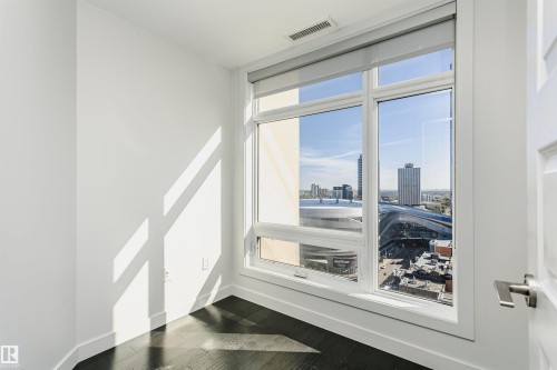 Expansive window offering urban scenery, dark wood-finish flooring, crisp white walls, and a modern door with brushed nickel hardware - #1902 10388 105 St Nw, Edmonton, AB 