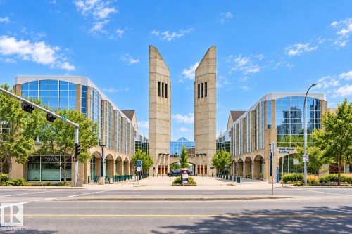 Modern architectural building with two prominent towers, expansive glass facades, arched ground-level walkways, and mature street trees - #1902 10388 105 St Nw, Edmonton, AB 
