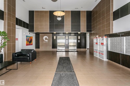 Lobby with neutral-toned tiled flooring, accent walls featuring dark and light-toned paneling, dual stainless steel elevators, and recessed lighting - #1902 10388 105 St Nw, Edmonton, AB 