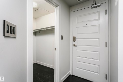 Panel-style entry door with smart lock, adjacent to a walk-in closet with dark wood-finish flooring and a clothing rod - #1902 10388 105 St Nw, Edmonton, AB 