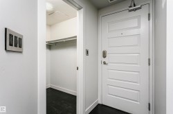 Panel-style entry door with smart lock, adjacent to a walk-in closet with dark wood-finish flooring and a clothing rod - 