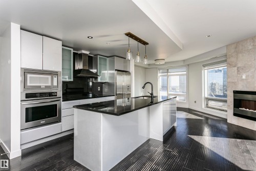 Gourmet kitchen featuring stainless steel appliances, dark stone countertops, white cabinetry, and an island with an integrated sink - #1902 10388 105 St Nw, Edmonton, AB 