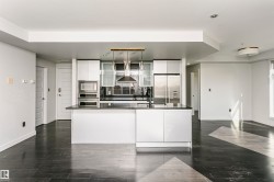 Modern kitchen featuring white cabinetry, a large island with dark countertop, and integrated stainless steel appliances - 