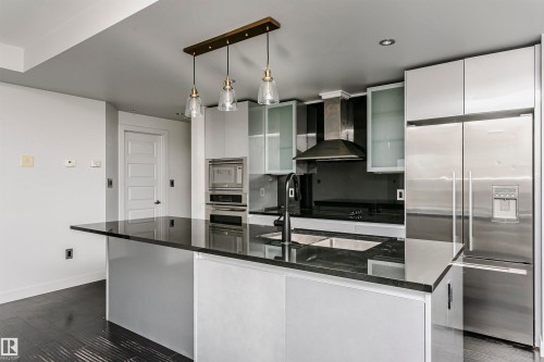 Kitchen featuring a black countertop island with double basin sink, stainless steel appliances, modern pendant lighting, and white cabinetry - #1902 10388 105 St Nw, Edmonton, AB 