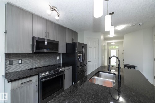 Kitchen featuring dark granite countertops, grey cabinetry, stainless steel appliances, a mosaic tile backsplash, and a large kitchen island with a double basin sink and gooseneck faucet - 1640 Chapman Way Sw, Edmonton, AB - Indoor Photo Showing Kitchen With Double Sink With Upgraded Kitchen