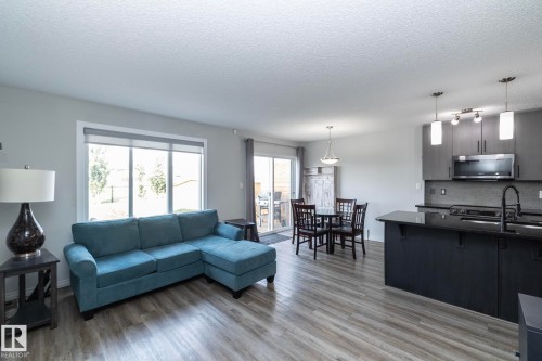 Open-concept living area featuring wood-finish flooring throughout, a kitchen island with a dark countertop, grey cabinetry, a stainless steel over-the-range microwave, and a glass sliding door - 1640 Chapman Way Sw, Edmonton, AB - Indoor