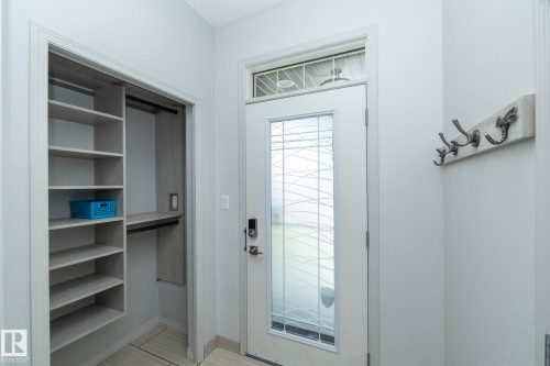 Entryway featuring a decorative glass door with transom window, light wood-finish flooring, and a built-in closet with shelving and hanging storage - 1640 Chapman Way Sw, Edmonton, AB - Indoor