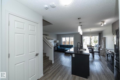 Open-concept living space featuring wood-finish flooring, a dark kitchen island with pendant lighting, a dining area with a sliding glass door, and a living area with large windows - 1640 Chapman Way Sw, Edmonton, AB - Indoor