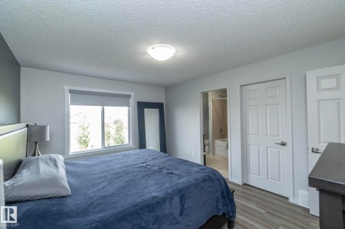 Bedroom featuring wood-finish flooring, light grey walls, and a large window with roller shade - 1640 Chapman Way Sw, Edmonton, AB - Indoor Photo Showing Bedroom
