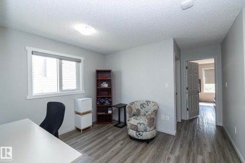 Light gray painted walls and wood-finish flooring define this room, featuring a large window with white trim, a flush-mount ceiling light fixture, and a paneled interior door - 1640 Chapman Way Sw, Edmonton, AB - Indoor Photo Showing Office