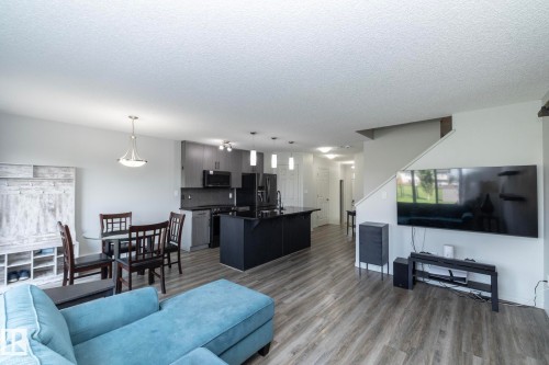 Open-concept living area featuring wood-finish flooring, a contemporary kitchen with dark cabinetry and countertops, a dining space with pendant lighting, and a staircase - 1640 Chapman Way Sw, Edmonton, AB - Indoor Photo Showing Living Room