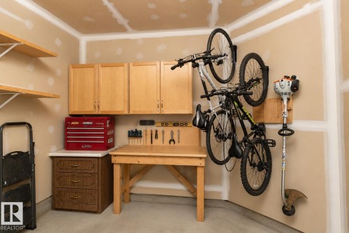 Dedicated garage space featuring built-in cabinetry, an integrated workbench, wall-mounted shelving, and a concrete floor - 1640 Chapman Way Sw, Edmonton, AB - Indoor Photo Showing Other Room