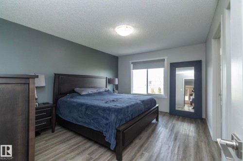 Bedroom featuring wood-finish flooring, a neutral wall color with an accent wall, a window with roller shades, and a flush-mount ceiling light - 1640 Chapman Way Sw, Edmonton, AB - Indoor Photo Showing Bedroom