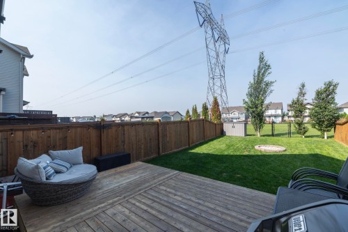 Expansive backyard featuring a wood-finish deck, surrounded by a tall privacy fence, and a manicured lawn with a built-in fire pit - 1640 Chapman Way Sw, Edmonton, AB - Outdoor