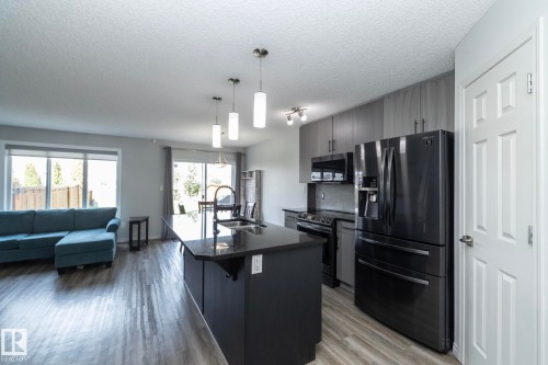 Open-concept kitchen featuring a dark cabinetry island with a black countertop and pendant lighting - 1640 Chapman Way Sw, Edmonton, AB - Indoor Photo Showing Kitchen With Double Sink