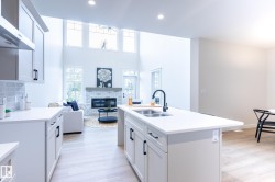 Kitchen island with dual basin sink and matte black faucet, light cabinetry with dark hardware, light wood-finish flooring, and a brick fireplace with a wood mantel - 