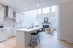 Open-concept living area featuring a kitchen island with seating, wood-finish flooring, a white brick fireplace, and high ceilings with transom windows - 