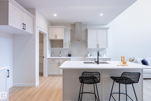 Kitchen featuring white shaker cabinetry, white countertops, stainless steel range hood, light wood-finish flooring, and recessed lighting - 6306 65 Ave, Beaumont, AB 