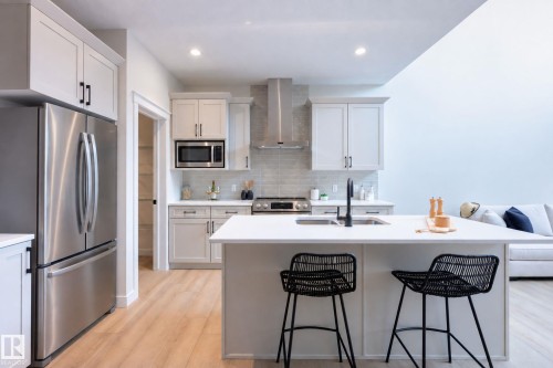 Kitchen featuring light-finish cabinetry, stainless steel appliances, a center island with sink, wood-finish flooring, and a tiled backsplash - 6306 65 Ave, Beaumont, AB 