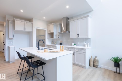 Kitchen with light wood-finish flooring, white cabinetry, integrated stainless steel range hood, light subway tile backsplash, and a central island with an undermount sink - 6306 65 Ave, Beaumont, AB 