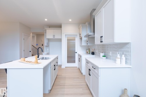 Spacious kitchen featuring white cabinetry, light-toned countertops, a center island with sink, stainless steel range hood, and light wood-finish flooring - 6306 65 Ave, Beaumont, AB 