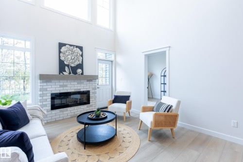 Vaulted ceiling with transom windows, contemporary electric fireplace with light brick surround and wood mantle, wood-finish flooring, and white interior walls - 6306 65 Ave, Beaumont, AB 