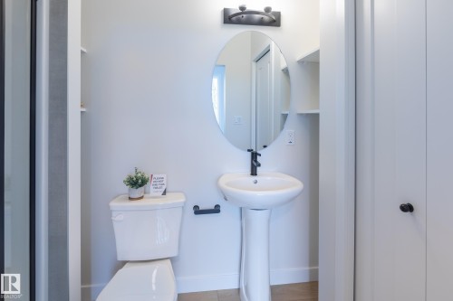 White pedestal sink with a matte black faucet, oval mirror, and wall-mounted vanity light - 6306 65 Ave, Beaumont, AB 