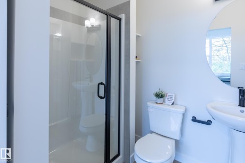 Glass-enclosed shower with black trim, pedestal sink with black faucet, toilet, and an oval mirror - 6306 65 Ave, Beaumont, AB 