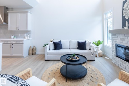 Vaulted ceiling with a large window, light wood-finish flooring, white brick-surround fireplace with a concrete mantle, and light-toned cabinetry with a subway tile backsplash - 6306 65 Ave, Beaumont, AB 